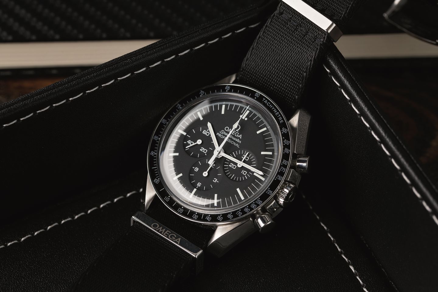 A close-up view of an Omega Speedmaster watch showcasing its black leather strap with white contrast stitching, emphasizing the strap's texture and craftsmanship against the watch's stainless steel case.