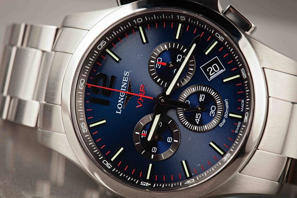 Close-up of a Longines VHP chronograph watch with a blue dial, featuring three subdials, red accents, and a stainless steel case and bracelet.