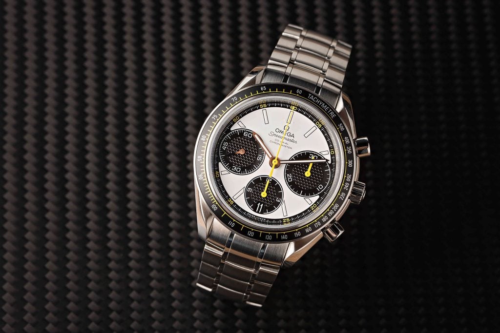 Omega Speedmaster chronograph watch with panda dial: white main dial, three black subdials, yellow chronograph hands, tachymeter bezel, and stainless steel case and bracelet. Close-up view against a textured dark background