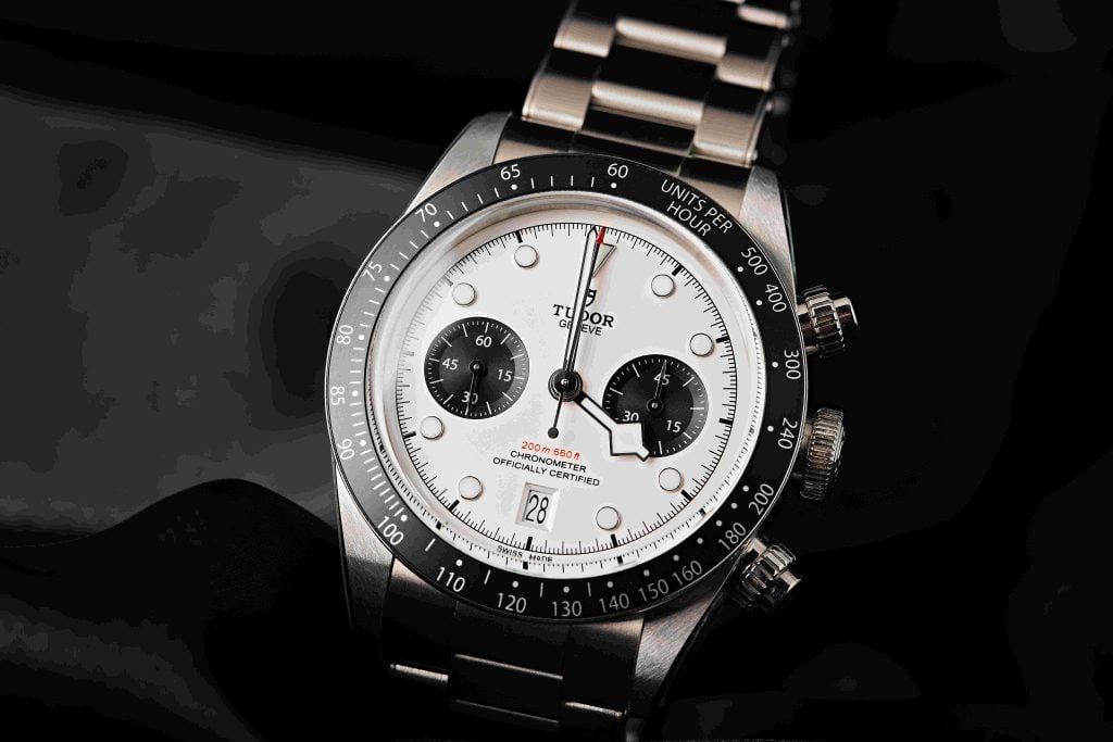 Close-up of a Tudor Black Bay Chrono watch, featuring a stainless steel case, white "panda" dial with black subdials, and a tachymeter bezel, photographed on a dark background.