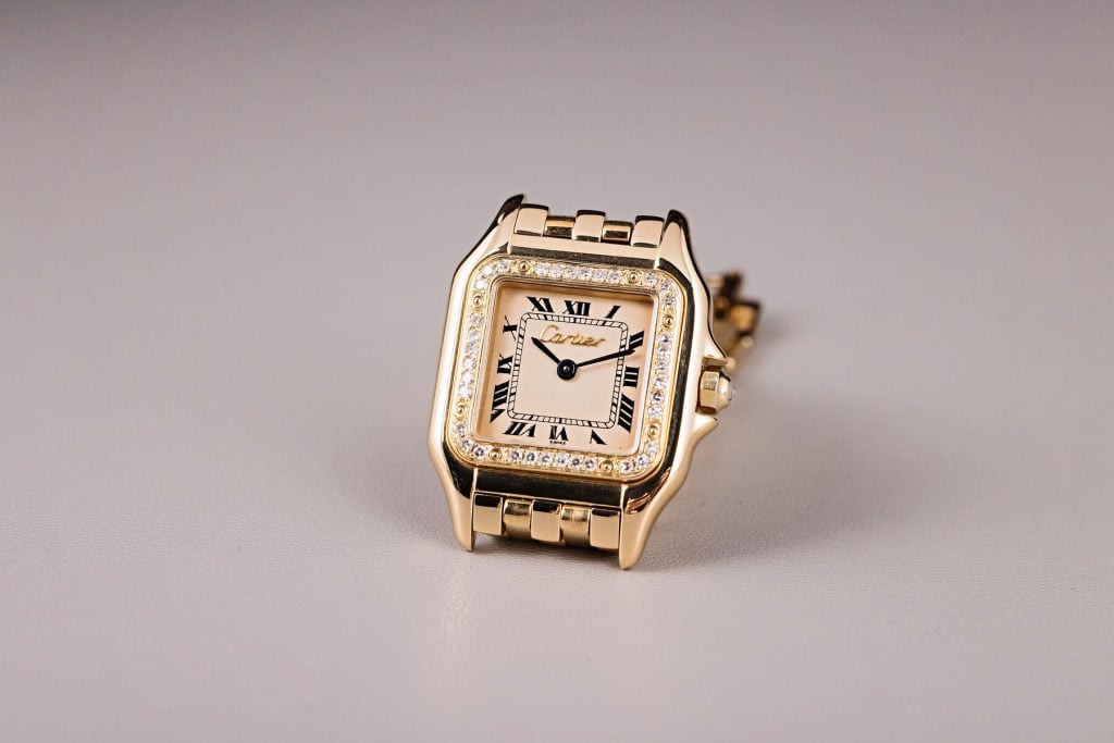 Cartier Panthère watch in yellow gold with a square case, Roman numeral dial, diamond-set bezel, and signature chain-link bracelet, elegantly displayed on a neutral background.