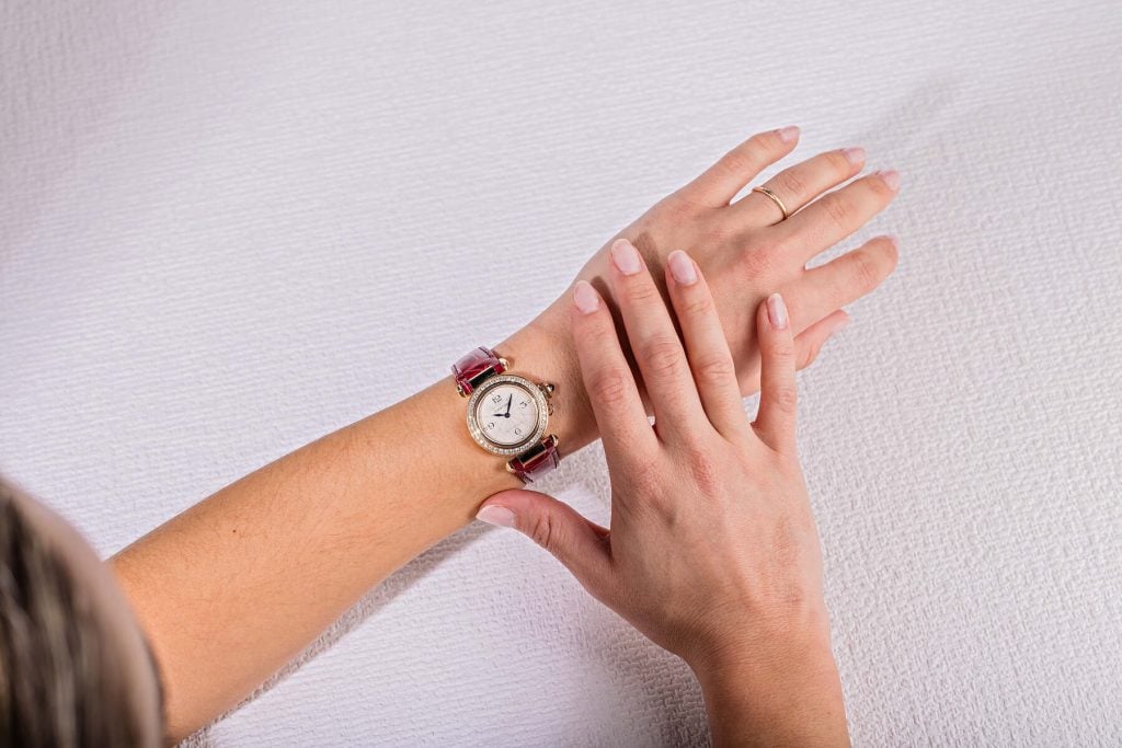 Cartier Pasha watch with a diamond-set bezel and red leather strap, worn on a woman’s wrist, displayed on a textured white background.